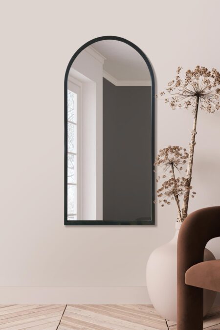 Tall arched black-framed mirror displayed indoors beside a dried flower arrangement