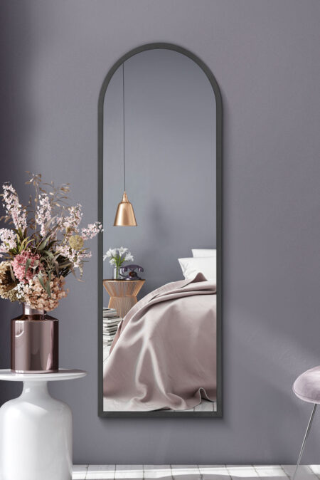 Tall arched grey-framed mirror displayed on a bedroom wall beside dried flowers