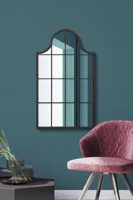 Cathedral-top window mirror with dark metal frame hung in a teal living room