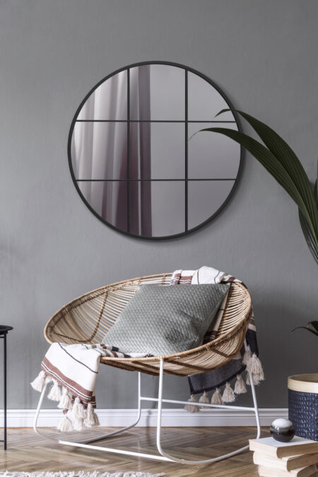 Large circular grid mirror above a rattan chair in a contemporary grey living room