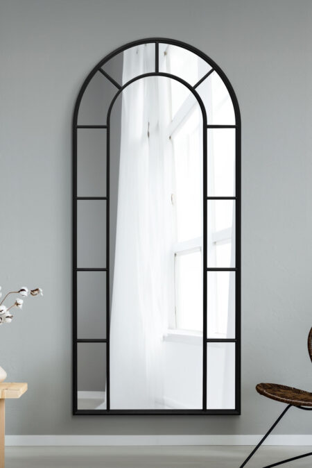 Tall black arched window-pane mirror leaning against a light grey interior wall