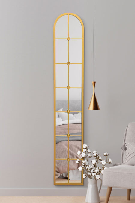 Tall gold arched windowpane mirror hung in a bedroom styled with cotton flowers and a pendant light