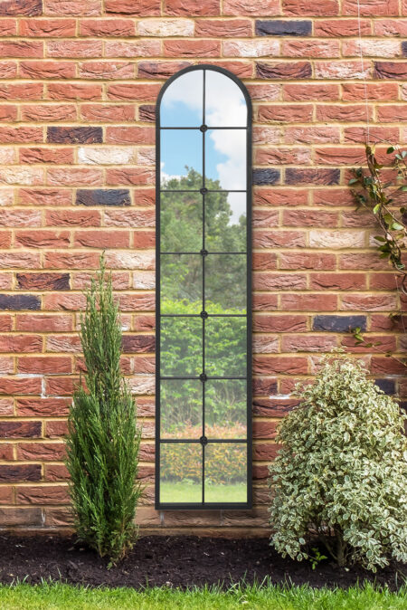 Tall black metal mirror full length arched window pane style mounted on an outdoor brick wall