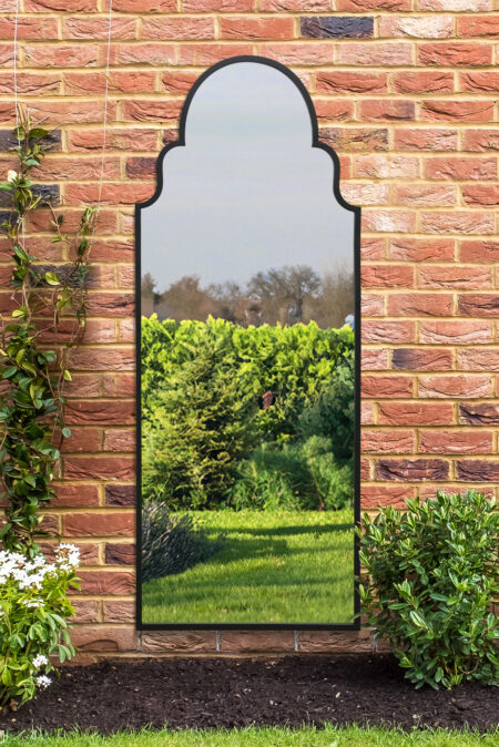Black scalloped arch full length mirror mounted on an outdoor red brick garden wall