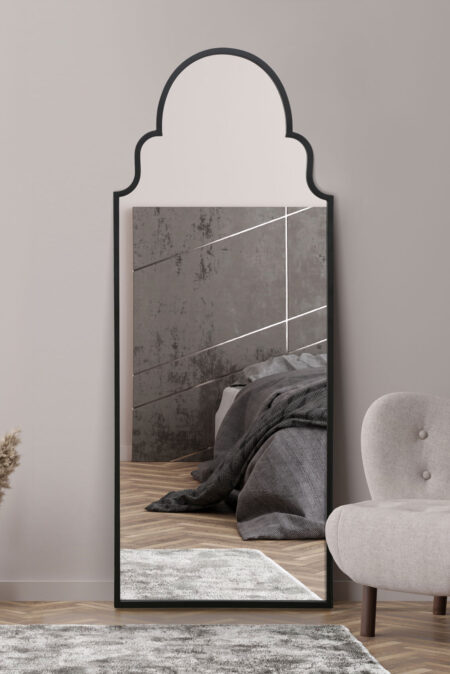 Tall Moorish arch mirror with slim black frame leaning against a bedroom wall