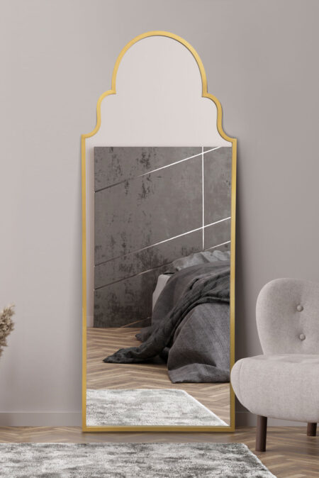 Full-length scalloped arch mirror with brushed gold frame leaning against a bedroom wall