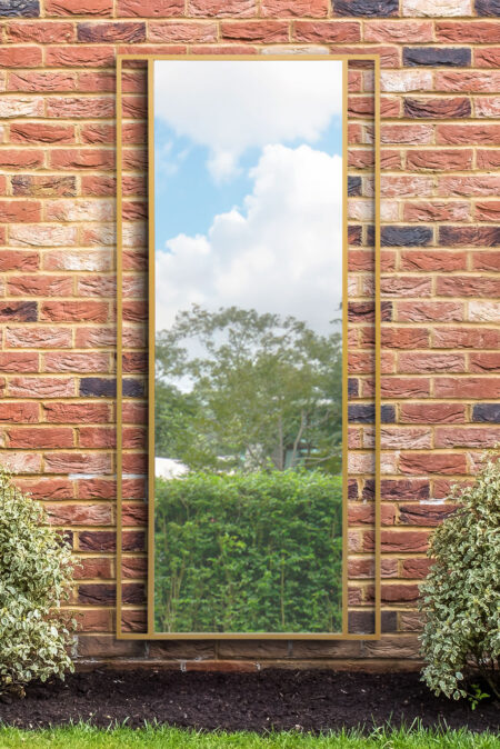 Full length wall mirror gold trim leaning against a red brick garden wall