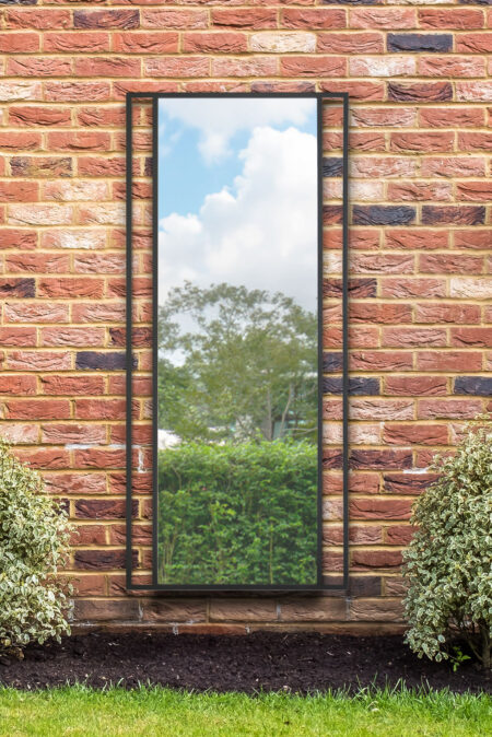 Full length mirror black metal frame mounted on an outdoor red brick garden wall