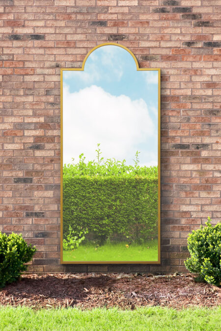 Gold arch topped wall mirror with satin frame leaning against an outdoor brick wall