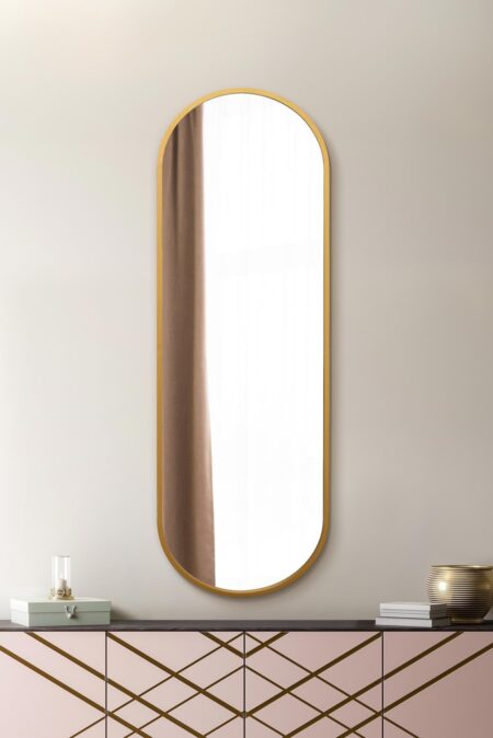 Tall capsule-shaped mirror with a brushed gold frame displayed above a pink Art Deco sideboard