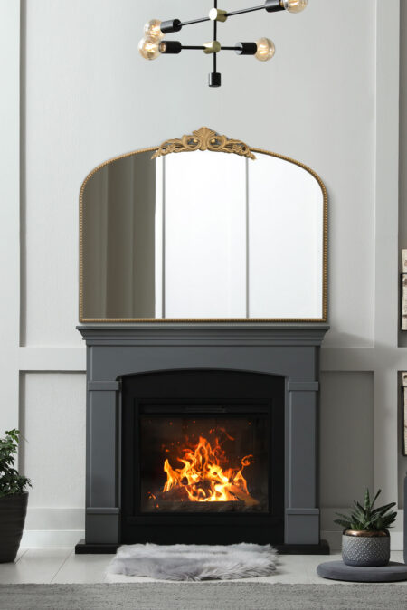 Gold ornate arch mirror with beaded crest displayed above a lit fireplace in a grey living room