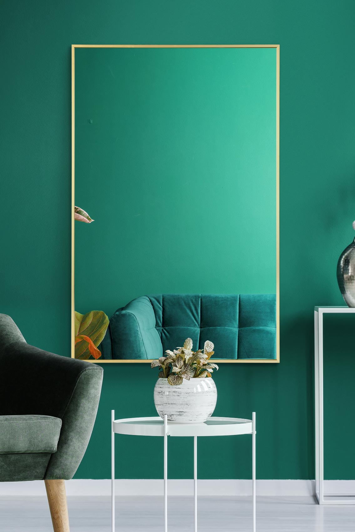 Large gold framed rectangular mirror leaning against a teal living room wall