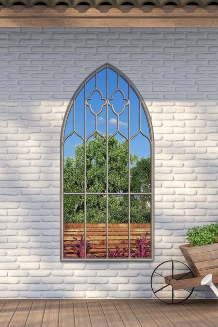 Large gothic arch garden mirror mounted on a white brick wall beside a wooden planter