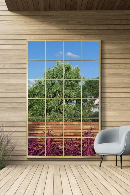Large gold window mirror with grid pane design leaning against a timber-clad garden wall