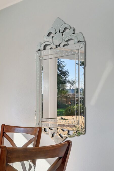 Venetian style mirror with etched floral crest hung above wooden dining chairs