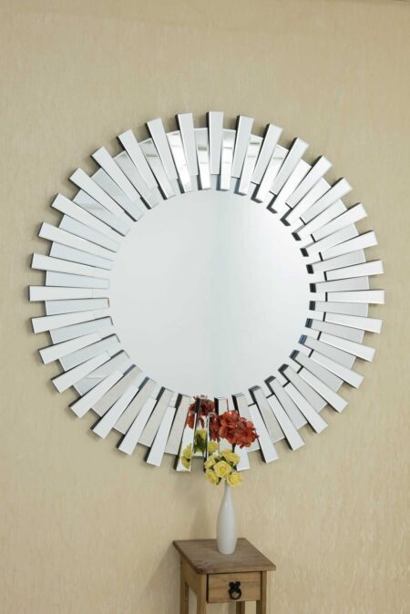 Round sunburst wall mirror displayed above a wooden side table with flowers beneath