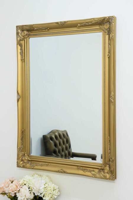 Ornate gold rectangular mirror with baroque carved frame hung on a white wall