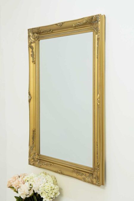 Large gold decorative wall mirror shown straight-on with pink flowers beneath