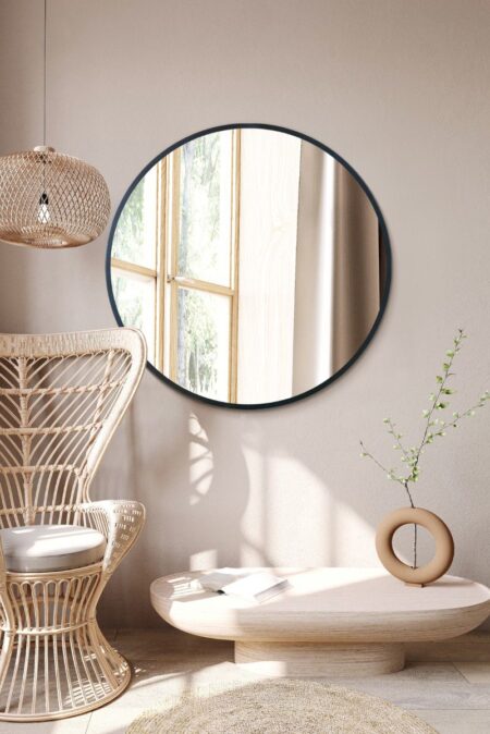 Large round black mirror hung above a rattan chair in a bright living room