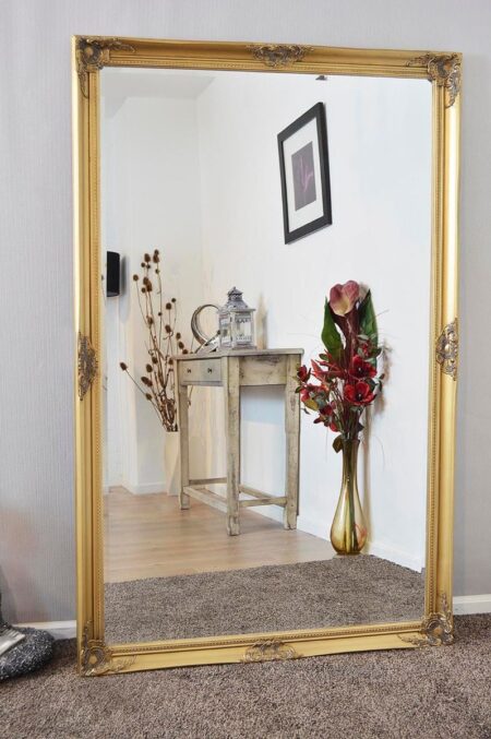 Large gold decorative wall mirror with ornate frame leaning against a grey wall